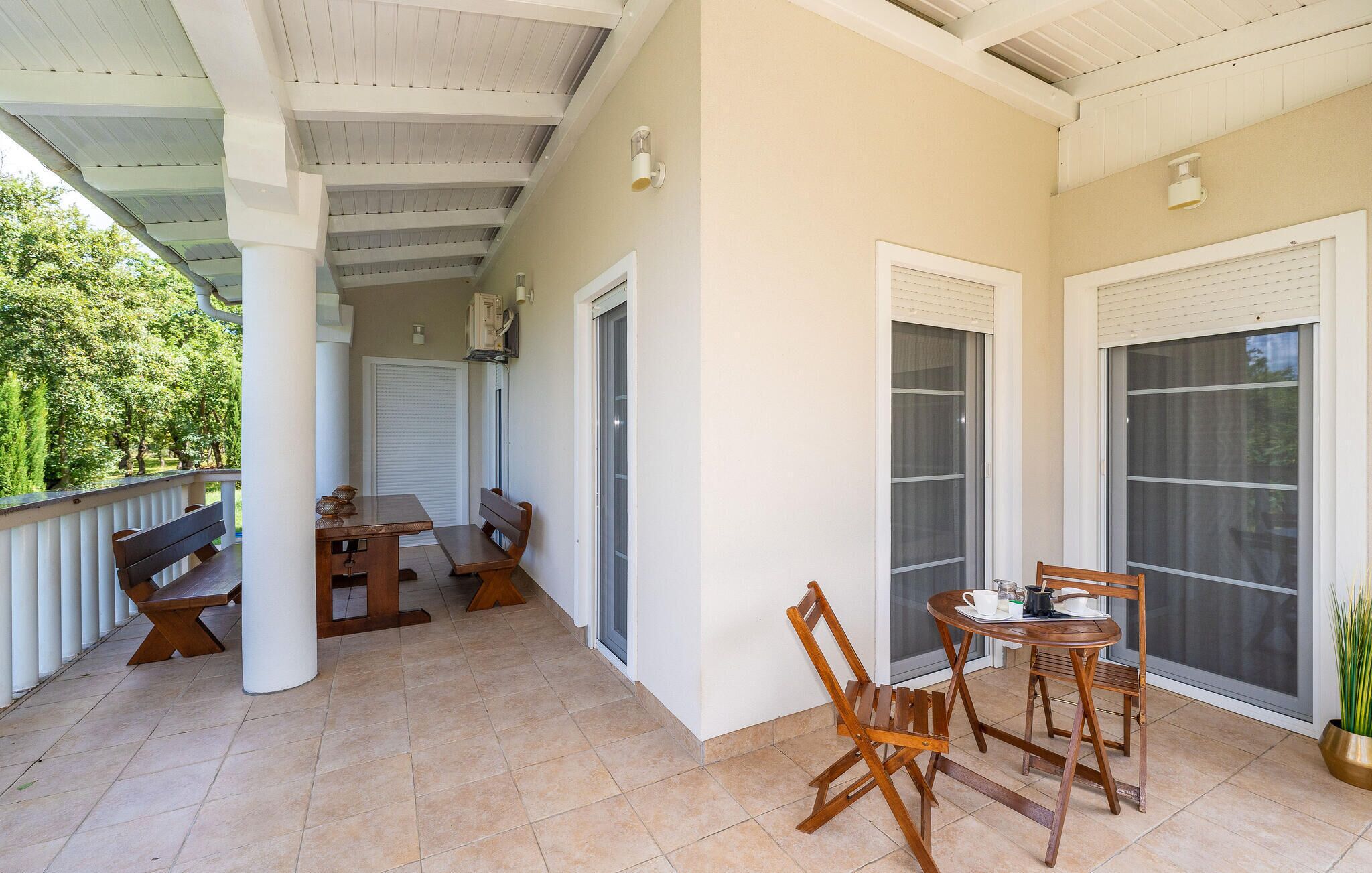 A covered patio area with a table and chairs, a bench, and a view of the outdoors.