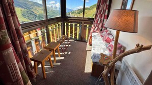A cozy room with a balcony, wooden furniture, and a view of the countryside. - Cozy 3-Room Apartment for 5 with Ski-In/Ski-Out, Balcony, and Modern Amenities (Les Menuires)