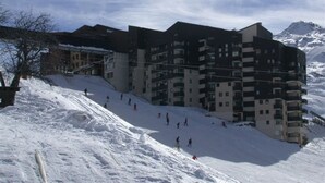 A multi-story building with a ski slope in front. - Cozy 3-Room Apartment for 5 with Ski-In/Ski-Out, Balcony, and Modern Amenities (Les Menuires)