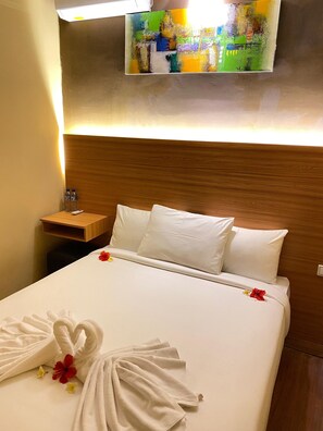 Une chambre d’hôtel avec un lit bien fait, une tête de lit en bois, une table de chevet avec une lampe et un tableau accroché au mur.