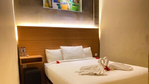Hotelkamer met houten hoofdeinde, een netjes opgemaakt bed met witte lakens, nachtkastje met waterflessen en een aan de muur bevestigde televisie.