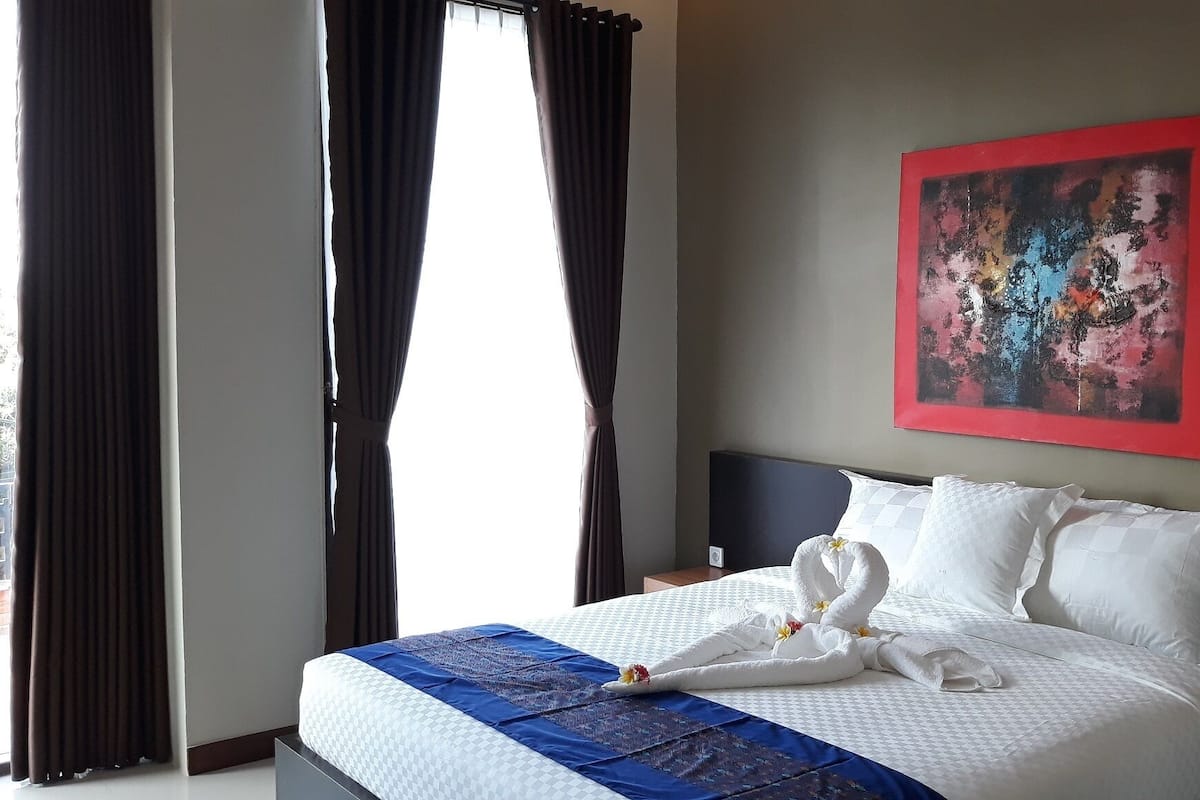 A hotel room with a bed, a painting, and a window with curtains.