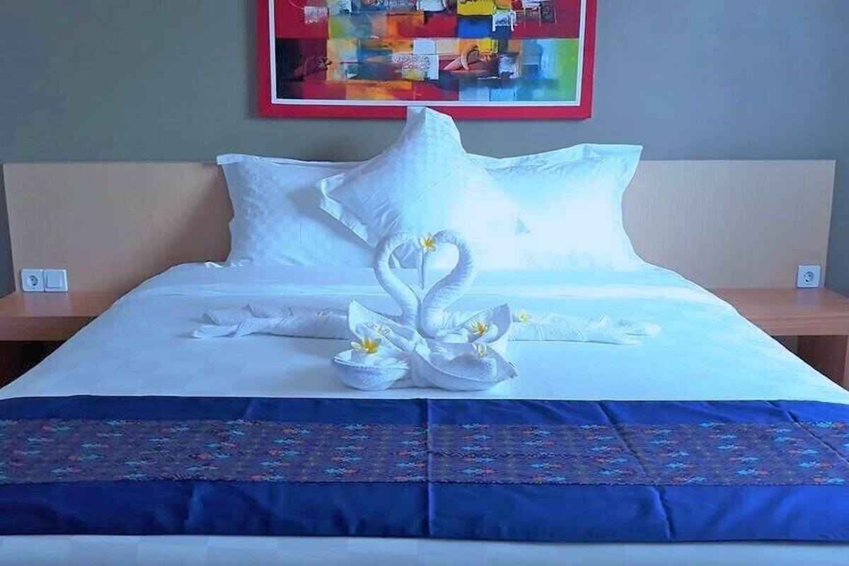 A neatly made bed with a blue bedspread and a decorative swan pillow arrangement.