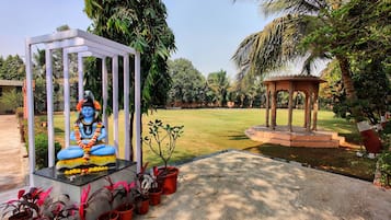 Surrounded by lush greenery, a serene statue sits within a tranquil pavilion, accompanied by a traditional gazebo.