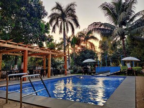 A pool area with a wooden pergola, lounge chairs, and umbrellas. - Pushp Vatika Resort & Lawns (Panvel)