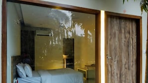 Un dormitorio con cama, almohadas, una mesita de noche y un ventanal que da a otra habitación y una puerta.