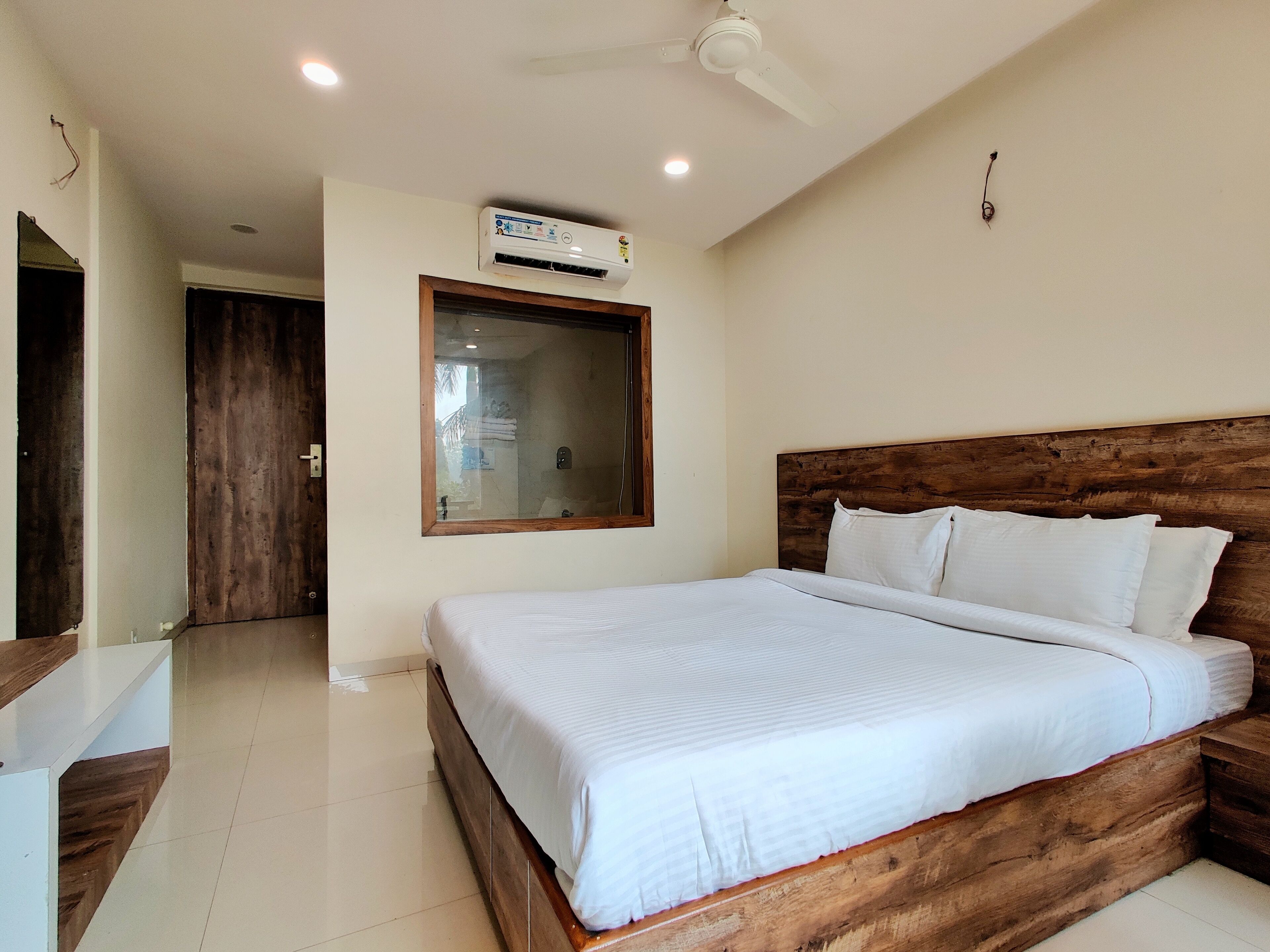 Ein Schlafzimmer mit einem hölzernen Kopfstück, einem großen Bett mit weißer Bettwäsche, einem Deckenventilator und einer Klimaanlage.