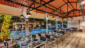 Un restaurante con terraza, piscina y una zona cubierta con plantas colgantes.