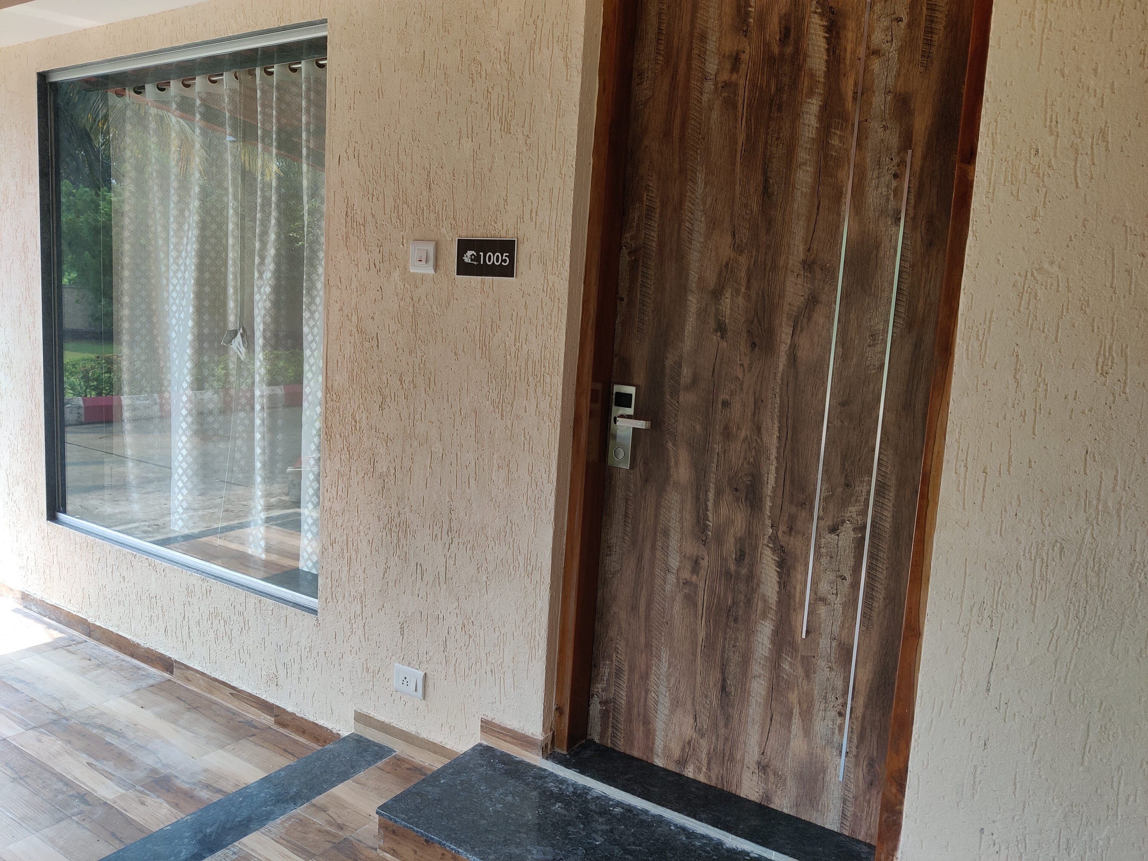 A wooden door with a number plate, a window with curtains, and a tiled floor.