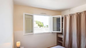 Une chambre à coucher avec un lit, une table de chevet avec une lampe, une fenêtre donnant sur un paysage dégagé et une armoire fermée par un rideau.