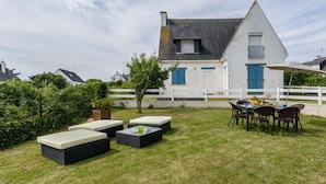 Une maison à l’extérieur blanc, avec un toit gris et des volets bleus. Une clôture blanche entoure la propriété.