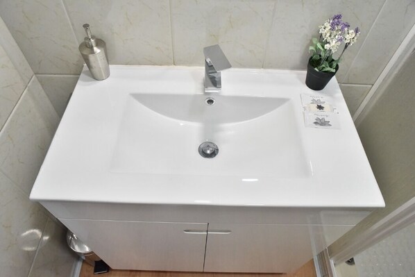 A bathroom with a white sink, a silver faucet, a potted plant, and a small card on the sink.