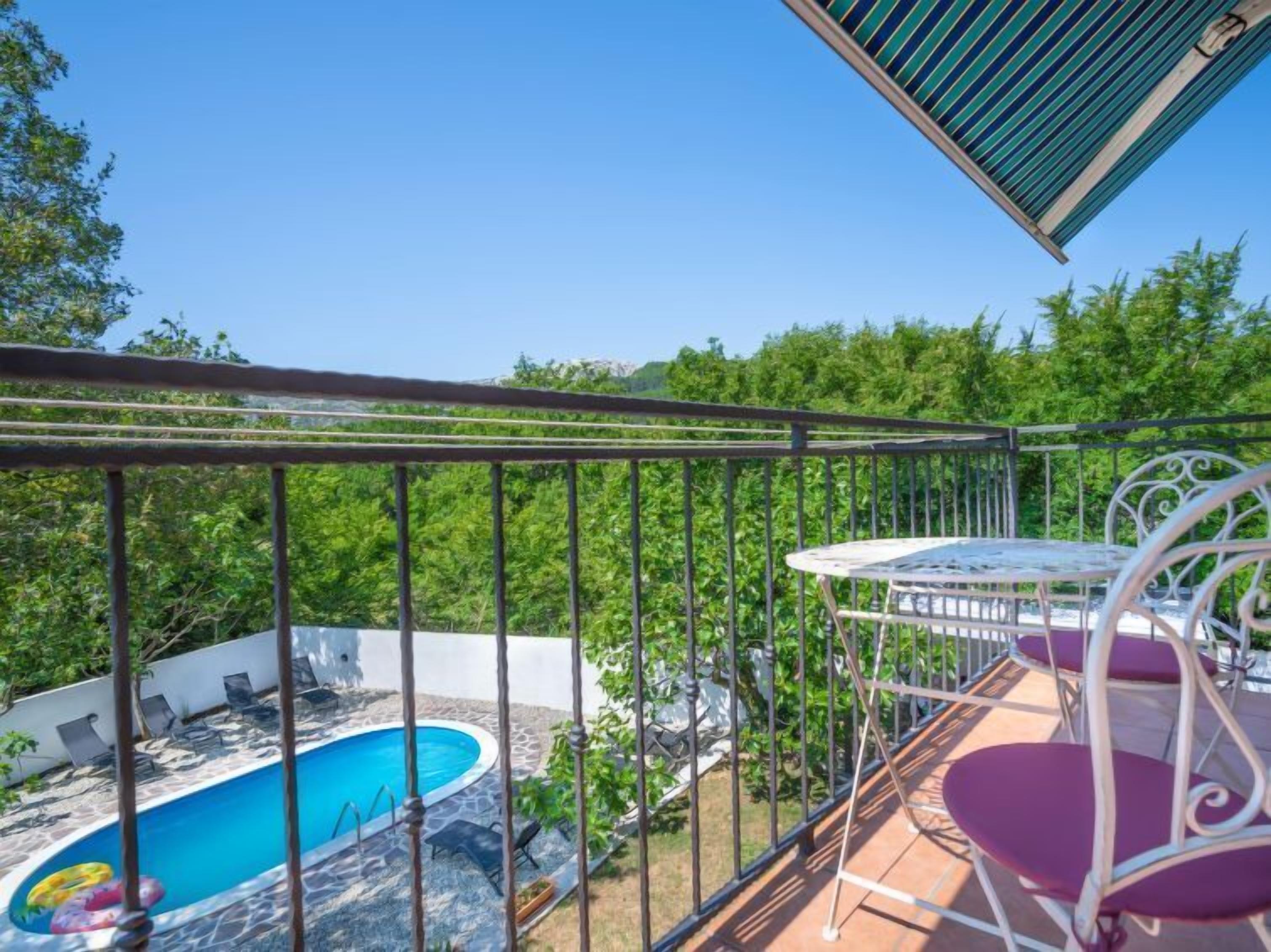 Un balcon avec une piscine, du mobilier d’extérieur et une vue sur la verdure.