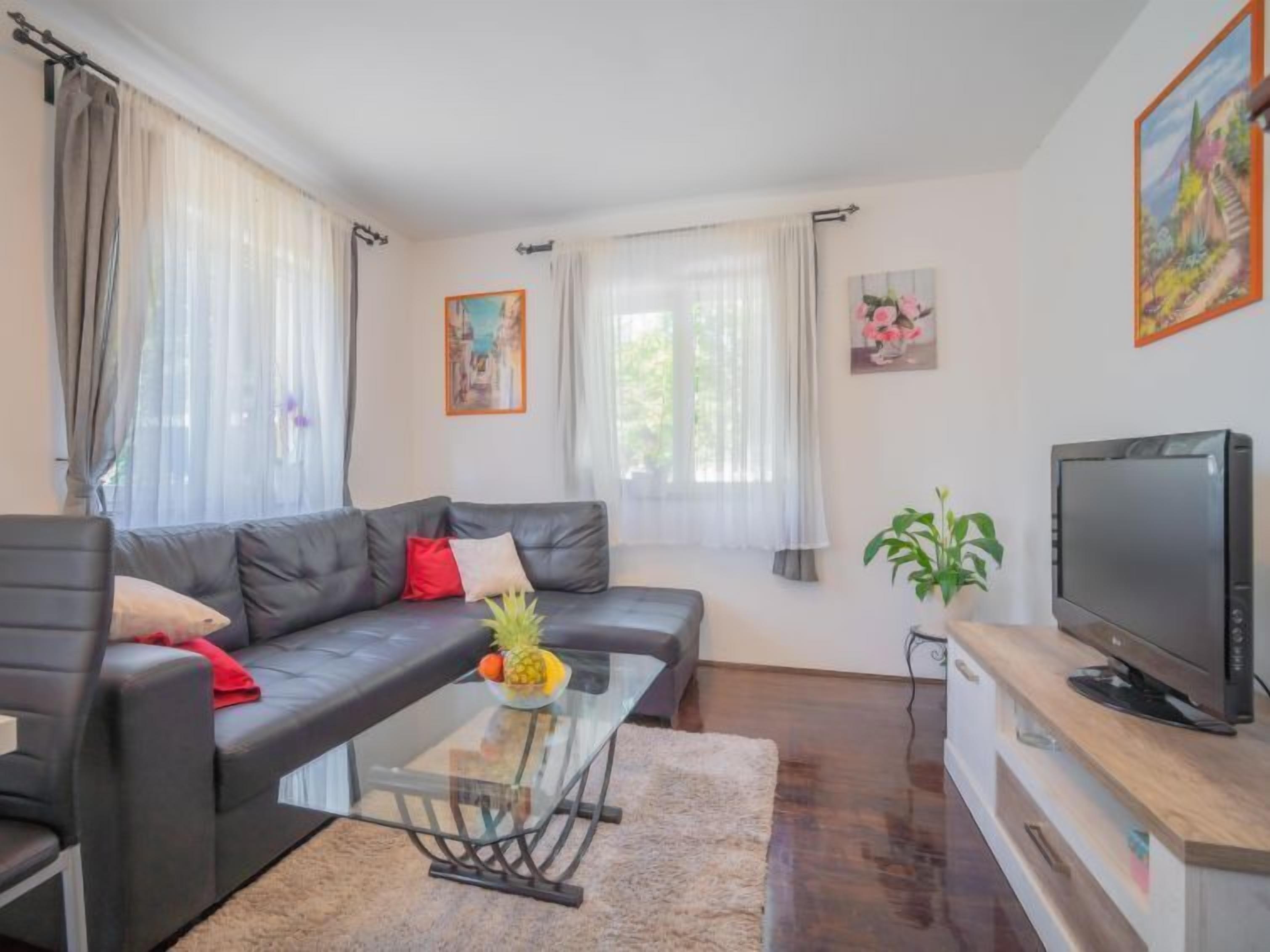 A modern living room with a leather sofa, glass coffee table, and a flat-screen TV on a wooden stand.