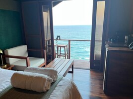 Una habitación con una cama, un banco de madera, una silla y vistas al océano.