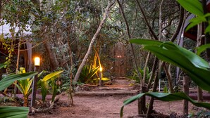 A forested area with a dirt path, wooden structures, and a sign indicating a restroom. - Sky Island Resort (Ponta d'Ouro)