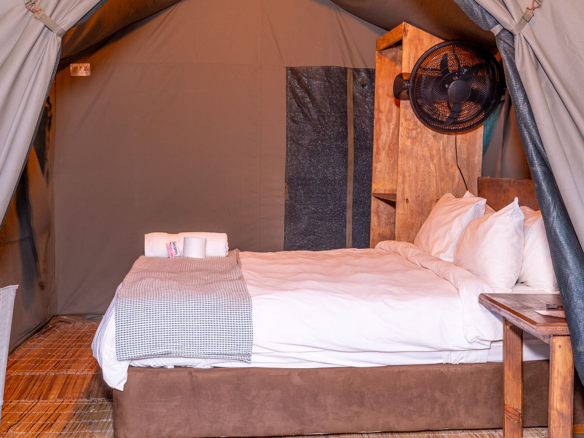 A tent with a bed, a fan, and a wooden headboard.