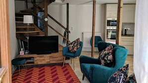Una sala de estar moderna con una escalera de madera, sillones color turquesa, un televisor de pantalla plana y un tapiz con estampado tipo espiga.