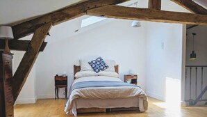 Un dormitorio con techo inclinado, vigas de madera, una cama con almohada estampada, dos mesitas de noche y un mueble auxiliar.