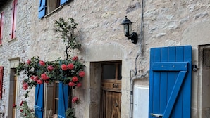 Un edificio de piedra con contraventanas azules, una puerta de madera y plantas en macetas.