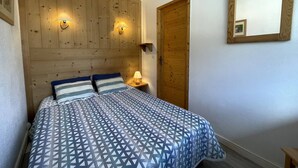 A bedroom with a wooden headboard, two bedside lamps, a bed with a patterned bedspread, and a wooden door. - Classic apartment for 4 at La Croisette (Les Menuires)