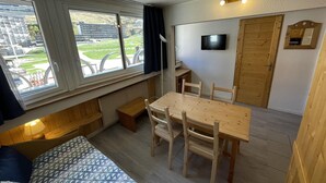 A compact room with a bed, a dining table with chairs, a TV, and a window with a view of buildings and greenery. - Classic apartment for 4 at La Croisette (Les Menuires)