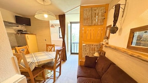 Een gezellige kamer met een eettafel, houten stoelen, een bruine bank, een televisie en houten wanddecoratie.