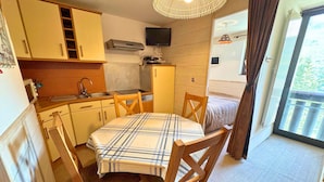 Een compacte keuken met een eettafel en stoelen, een televisie en een raam met gordijnen.