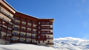 A multi-story hotel with balconies, set against a snowy mountain backdrop. - Charming Ski-In/Ski-Out Apartment for 5 with Balcony, Near Restaurants and Free Shuttle (Les Menuires)