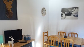 Ein Essbereich mit Holztisch und -stühlen, einem Fernseher auf einer Kommode sowie Wanddekorationen, darunter ein Hirschkopf und eine Uhr.