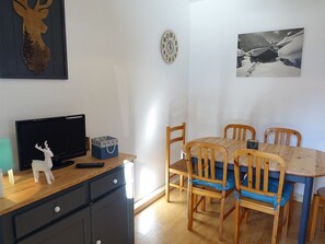 A dining area with a wooden table and chairs, a television on a cabinet, and wall decorations including a deer head and a clock.