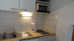 Eine kleine Küche mit Spüle, Herd, Kaffeemaschine und Mikrowelle.