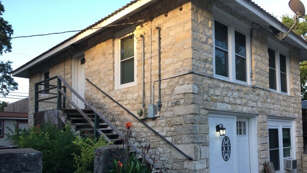 Un bâtiment en pierre avec une porte blanche, un escalier et une antenne parabolique.