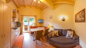 A cozy room with a wooden ceiling, a dining area with a table and chairs, a sofa with decorative pillows, and a television on the wall. - Apartment Tirol 75m² with 2BR, Balcony, Pool & Mountain View - near Skislope (St. Johann in Tirol)