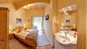A bedroom with a wooden bed, a bedside table with a lamp, a large mirror, and a bathroom with a sink and mirror. - Apartment Tirol 75m² with 2BR, Balcony, Pool & Mountain View - near Skislope (St. Johann in Tirol)