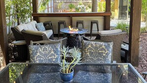 An outdoor patio with wicker furniture, a glass table, and string lights.