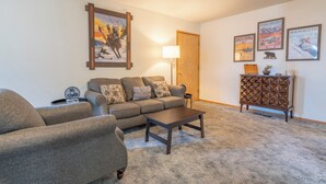 A living room with a sofa, armchair, coffee table, and a lamp. There are framed pictures on the wall and a small cabinet. - June Lake Lodge- Centrally located - short walk to JLB, The General Store, both Gull and June Lakes (June Lake)