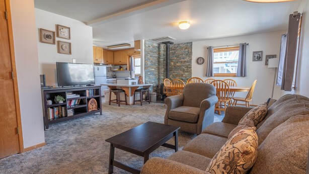 A living room with a sofa, armchair, and coffee table. There is a television on a stand, a bookshelf, and a dining area with chairs and a table. - June Lake Lodge- Centrally located - short walk to JLB, The General Store, both Gull and June Lakes (June Lake)