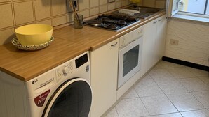 Pieni, käytännöllinen keittiö, jossa on pesukone, liesi ja ikkuna.