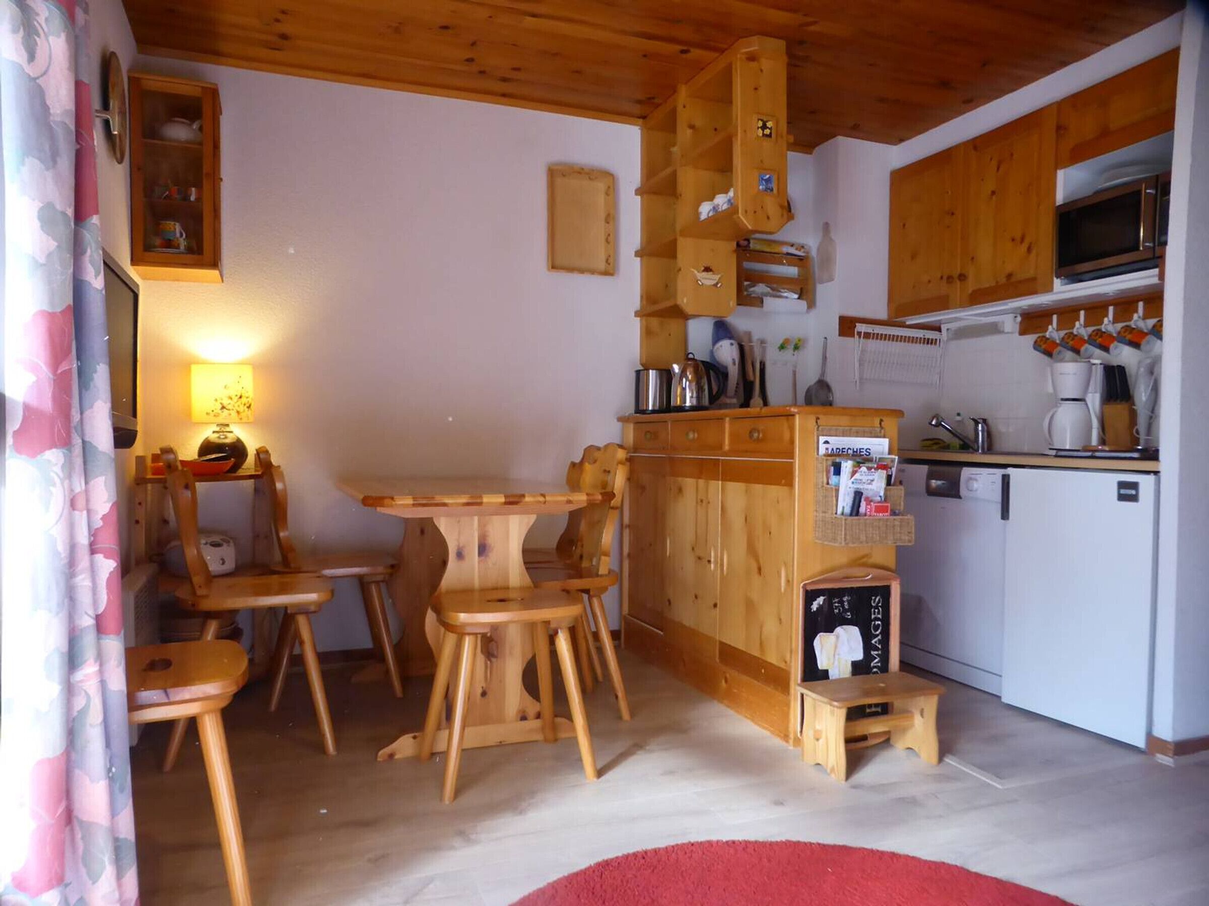 A wooden interior with a dining table, chairs, a kitchen area with a microwave, and a small refrigerator.