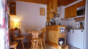 Een houten interieur met een eettafel, stoelen, een keukenhoek met een magnetron en een kleine koelkast.