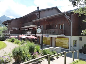 A wooden building with a balcony, outdoor seating, and signs for a restaurant and a sports store.