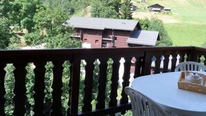 Een balkon met uitzicht op een bergachtig landschap, een houten hek en een tafel met een theepot.
