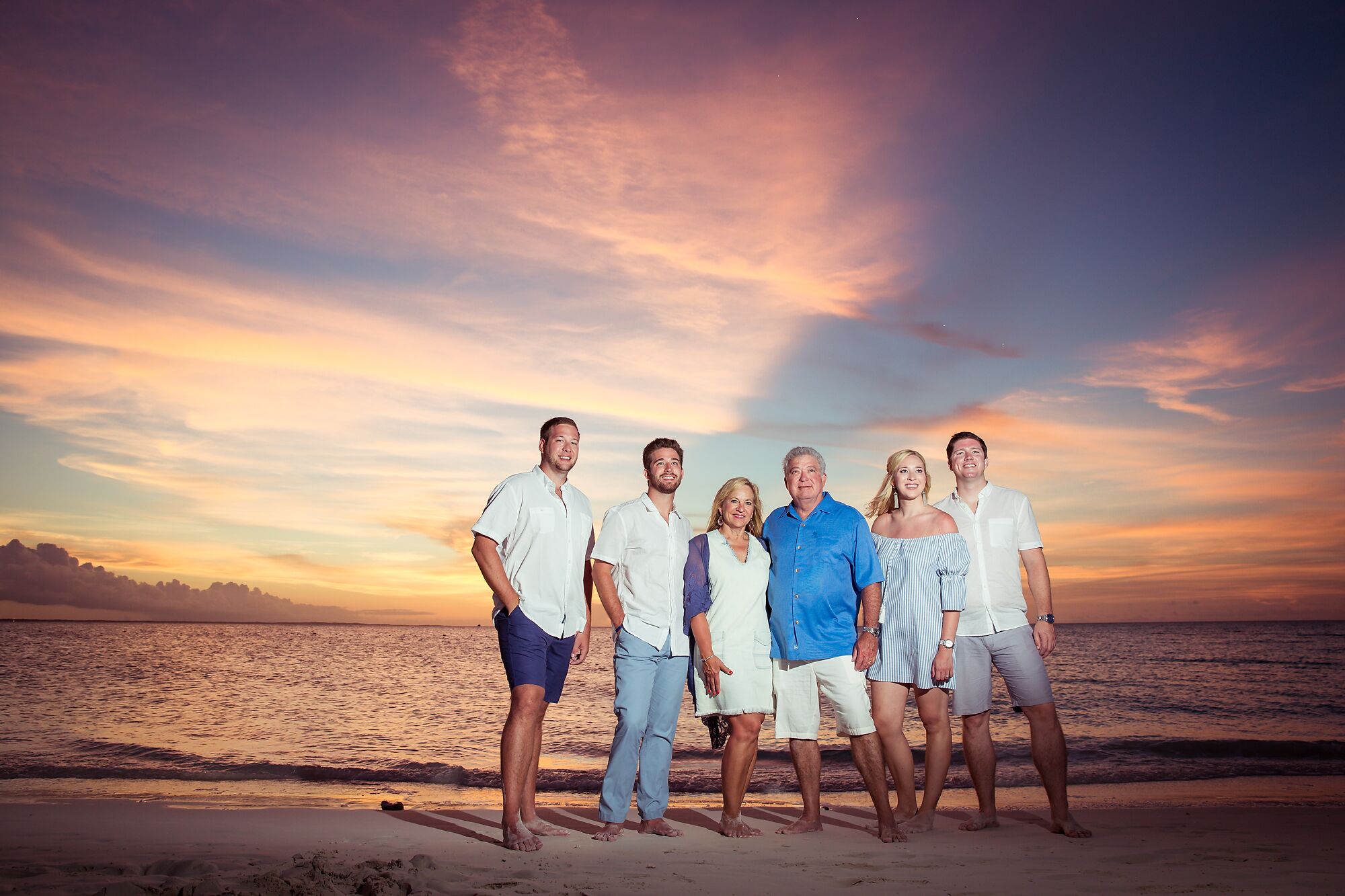 A group of people standing on a beach with a sunset in the background.