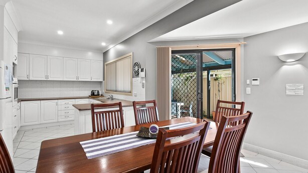 A modern kitchen with white cabinets, a dining area with a wooden table and chairs, and a sliding glass door leading to a patio. - 3-45 Park Street - Spacious Townhouse (EVANS HEAD)