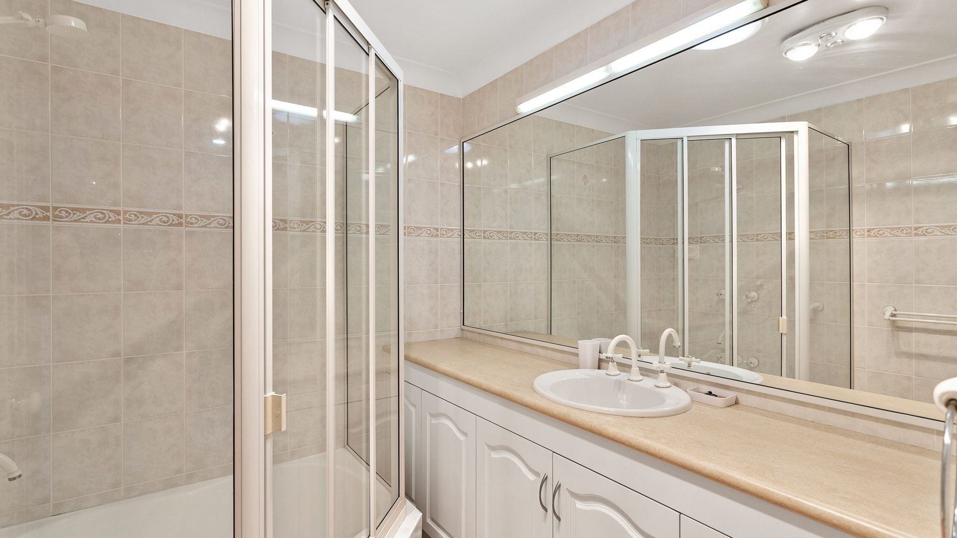 A modern bathroom with a glass shower enclosure, a sink with a mirror above it, and beige tiles.