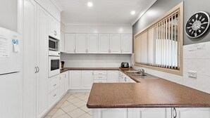 A modern kitchen with white cabinets, a granite countertop, a built-in oven, a microwave, and a clock on the wall. - 3-45 Park Street - Spacious Townhouse (EVANS HEAD)