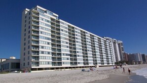 Un hotel de varios pisos con diseño moderno, situado junto a una playa de arena.