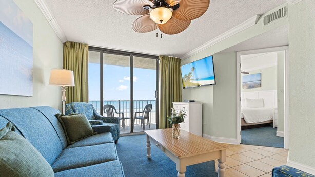 Una habitación con sofá, mesa, televisión y balcón con vistas.