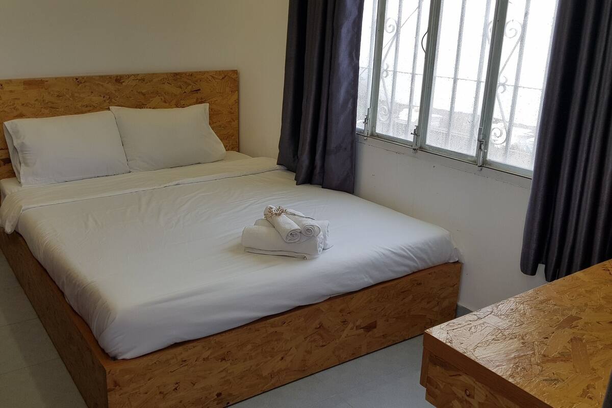 A neatly made bed with white linens, a wooden headboard, and a small wooden table beside it.